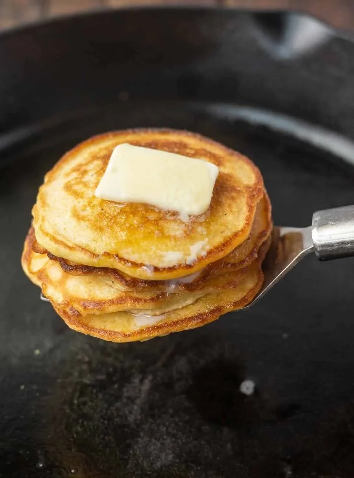 Plate of golden brown Johnny Cakes served with syrup and fresh fruit