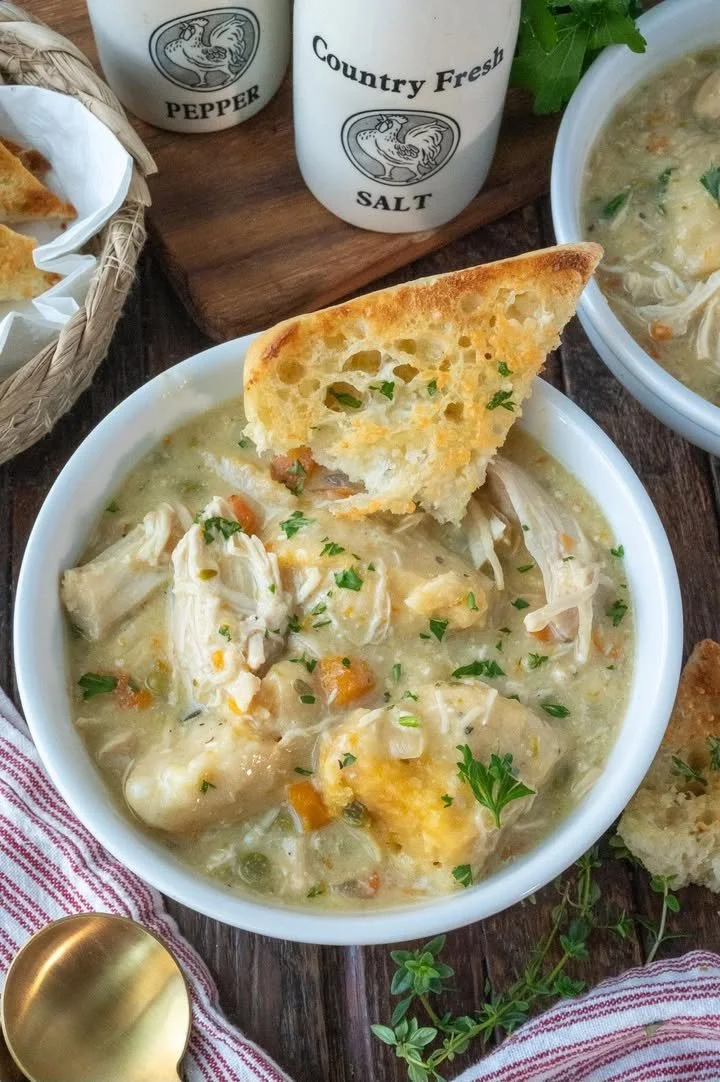 Slow Cooker Chicken and Dumplings Bowl of slow cooker chicken and dumplings served with fresh herbs.
