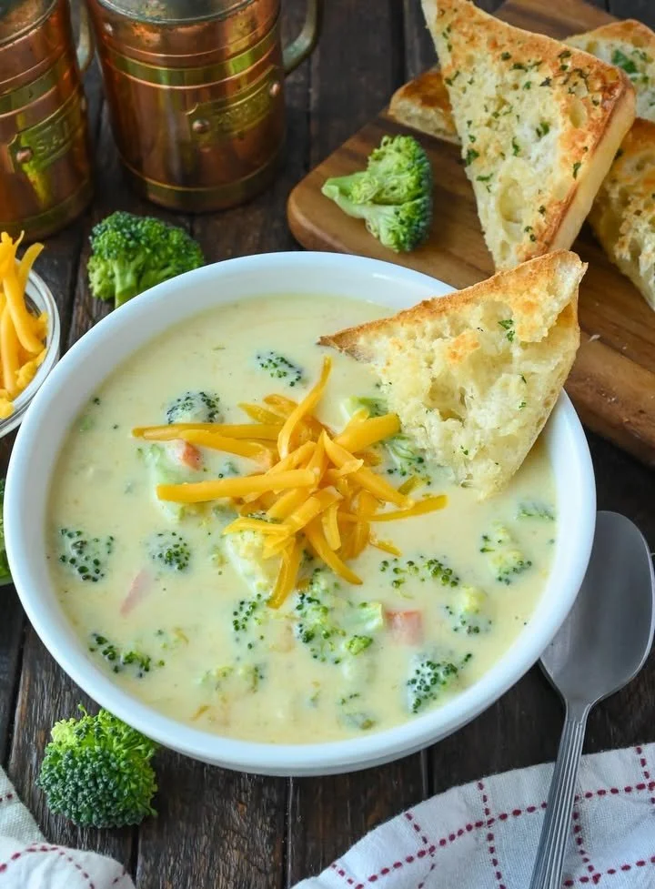 Bowl of creamy copycat Panera broccoli cheese soup garnished with cheese and broccoli florets.