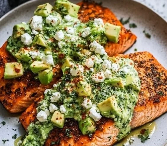 Baked salmon topped with avocado and feta cheese on a white plate